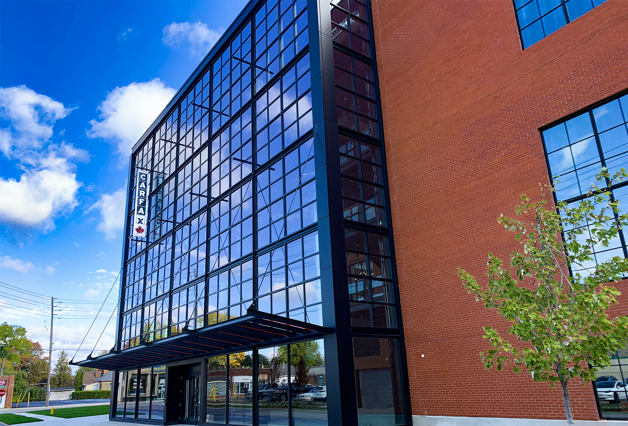 Photograph of CARFAX Canada’s corporate office entrance with a CARFAX Canada sign hanging from it and a red brick building is connected to the right.